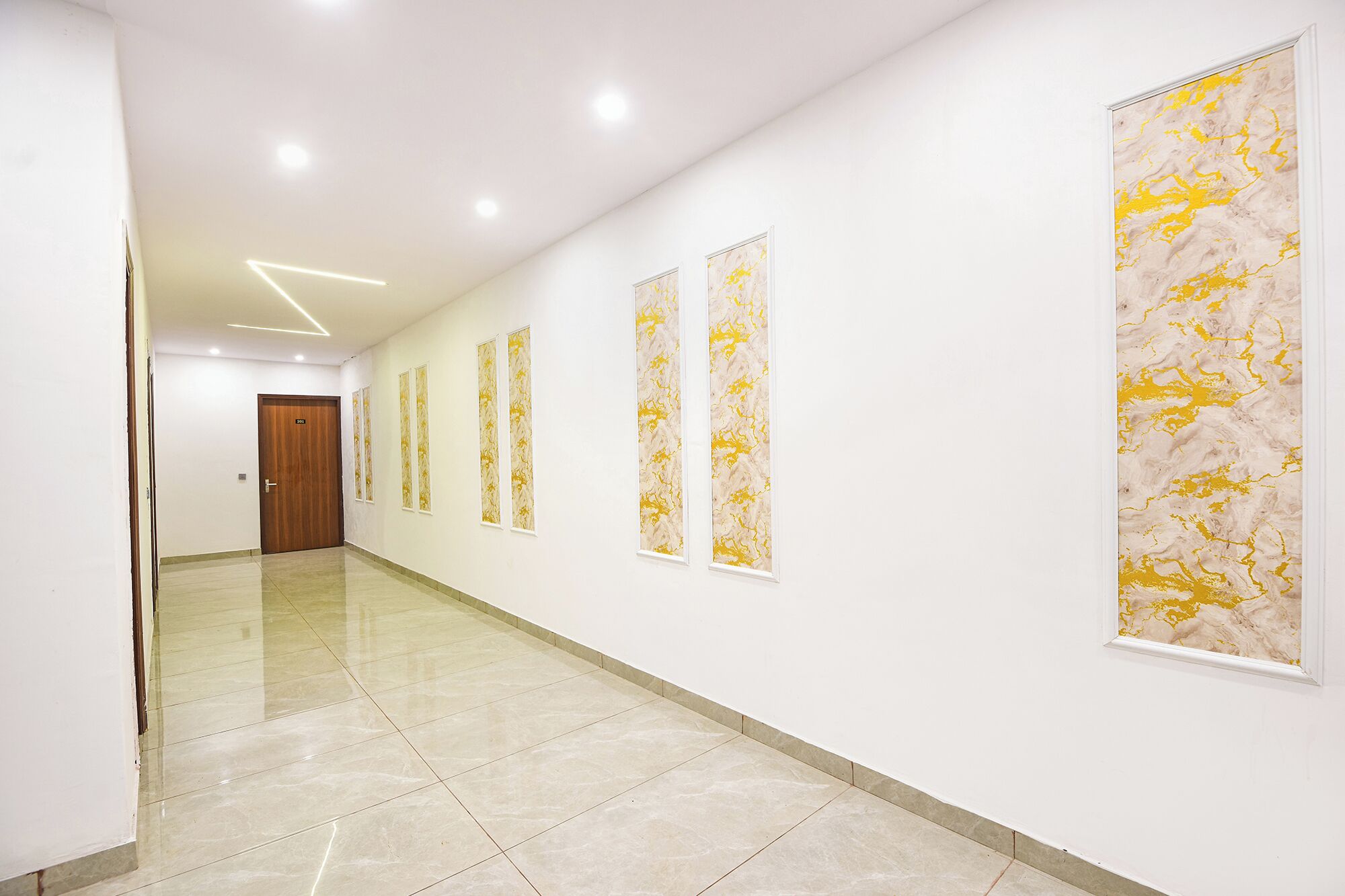 Un pasillo con una puerta de madera al final, paredes blancas y una serie de obras de arte verticales.