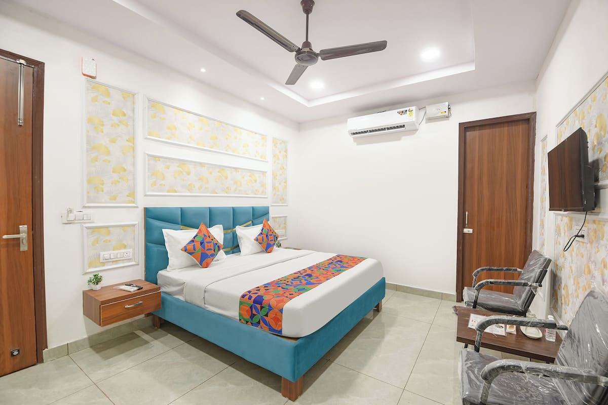 A bedroom with a bed, a ceiling fan, an air conditioner, a TV, and a desk with chairs.