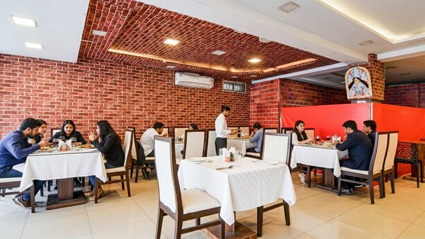A restaurant with brick walls, white tables, and chairs. - Fabhotel Rose (Barasat)