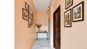 A hallway with a marble floor, framed artwork on the walls, a console table with a vase and candle, and a wooden door. - Fabhotel Rose (Barasat)