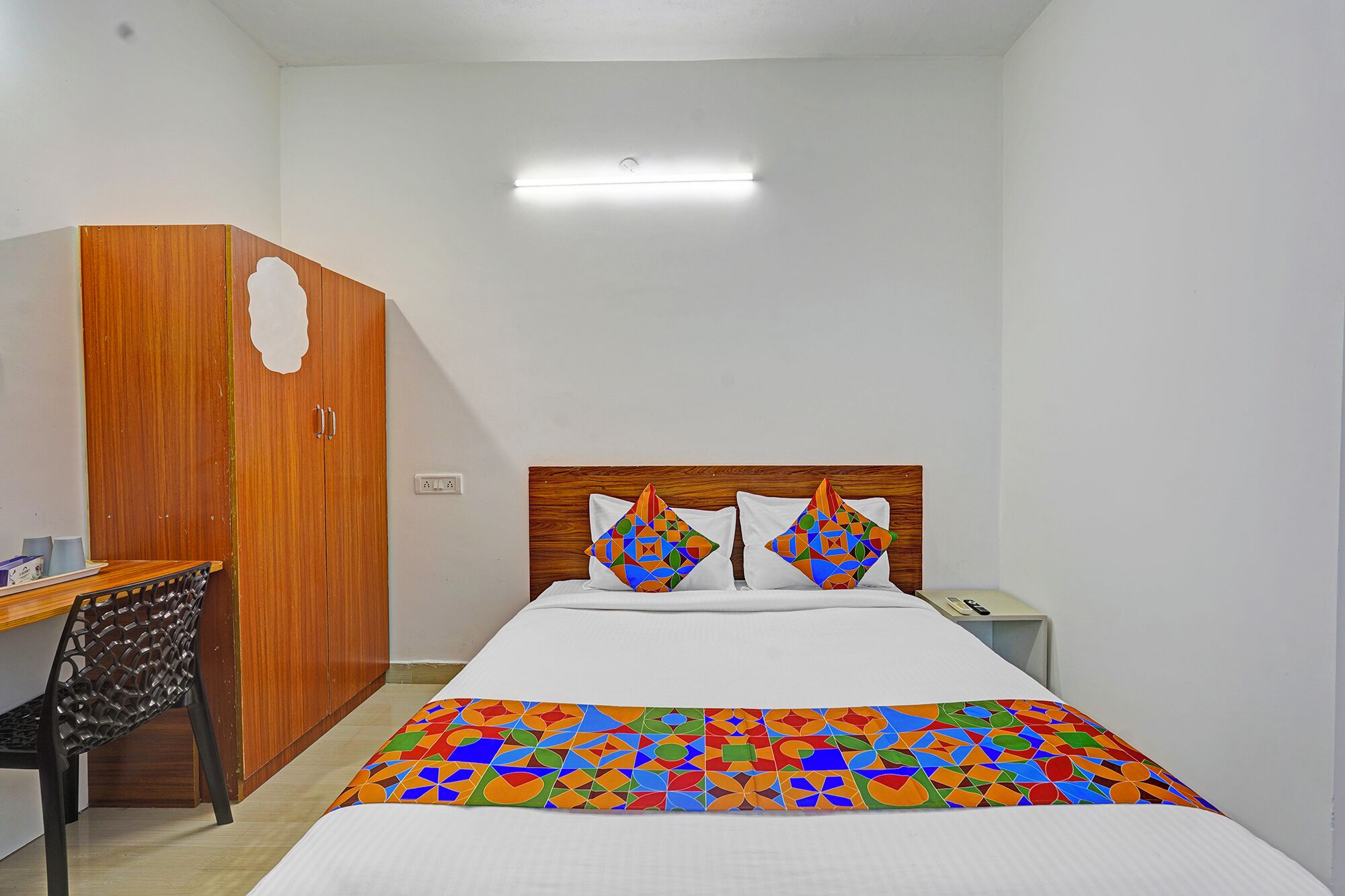 Una habitación de hotel con una cama, un armario de madera, un escritorio con una silla y una mesita de noche.