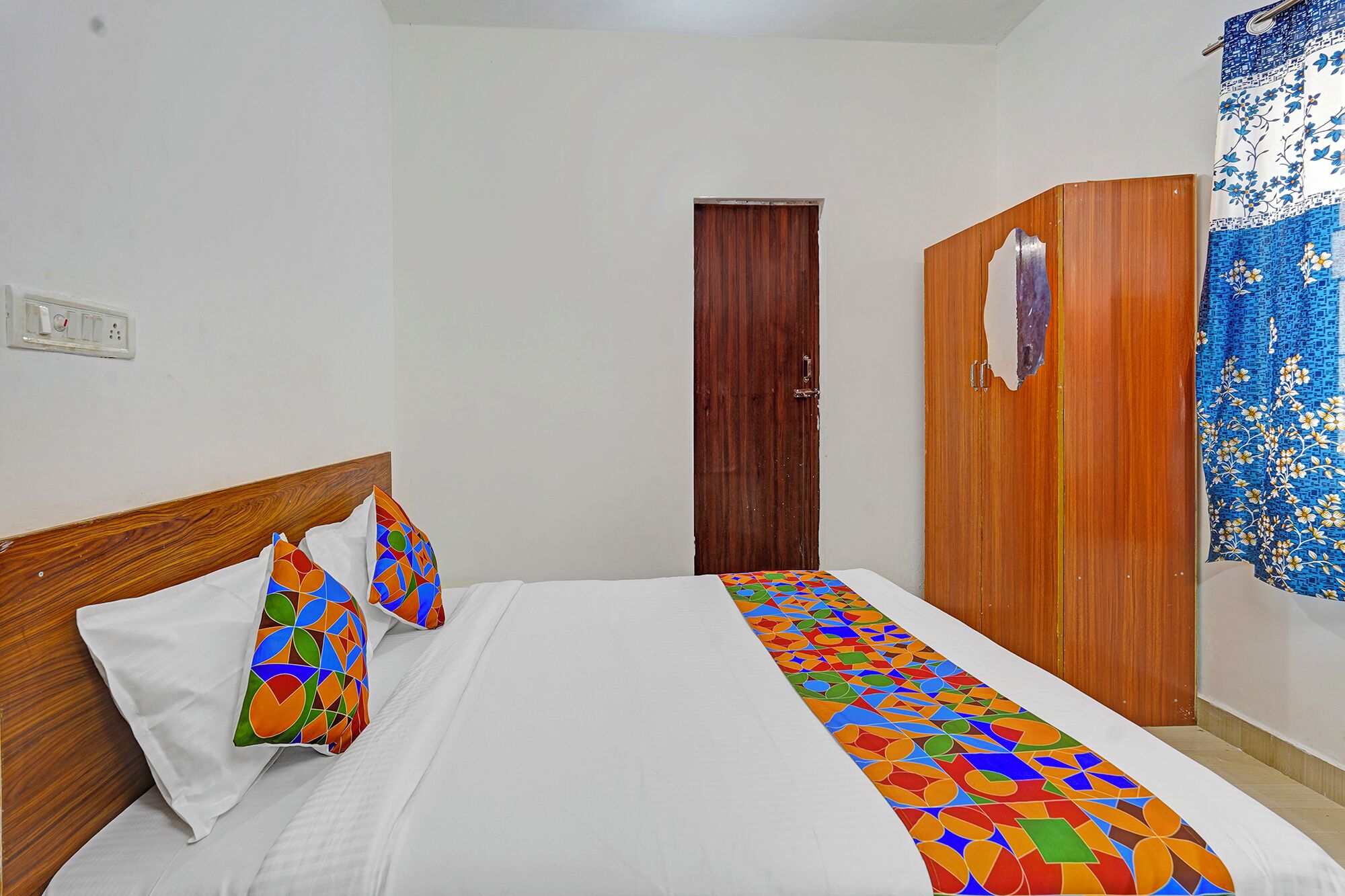 A hotel room with a bed, a wooden wardrobe, a door, and a curtain.