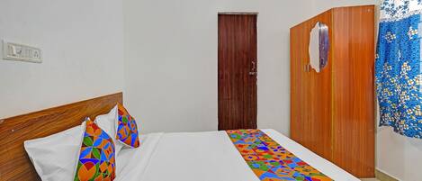 A hotel room with a bed, a wooden wardrobe, a door, and a curtain.