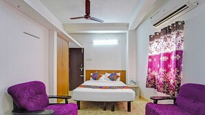 A hotel room with a bed, two purple armchairs, a nightstand, a ceiling fan, an air conditioning unit, and a door. - Fabexpress Ss Residency (Chennai)