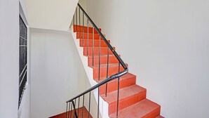 A staircase with red steps and black handrails, leading to a landing with a white wall and a metal gate. - Fabexpress Ss Residency (Chennai)