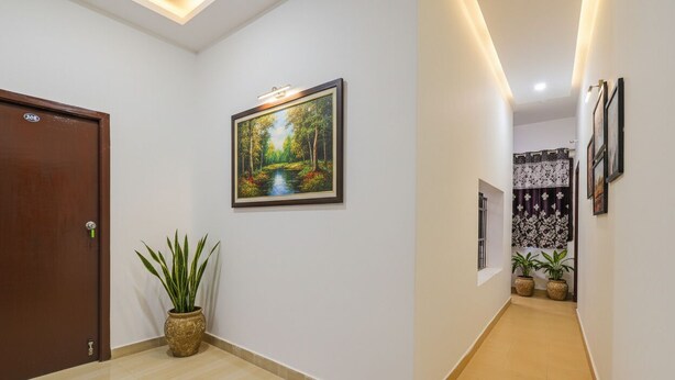 A hallway with a wooden door, a framed painting of a forest scene, and potted plants. - Fabexpress Ss Residency (Chennai)