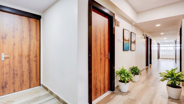 A hallway with wooden doors, potted plants, and framed artwork on the walls. - Fabhotel Sri Lakshmi Sea Grand (Visakhapatnam)