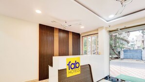 A reception area with a modern design, featuring a reception desk with a logo, a ceiling fan, and a view of the street outside. - Fabhotel Sri Lakshmi Sea Grand (Visakhapatnam)