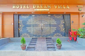 De ingang van Hotel Dream Villa met een grote decoratieve deur, een brandblusser en twee potplanten.
