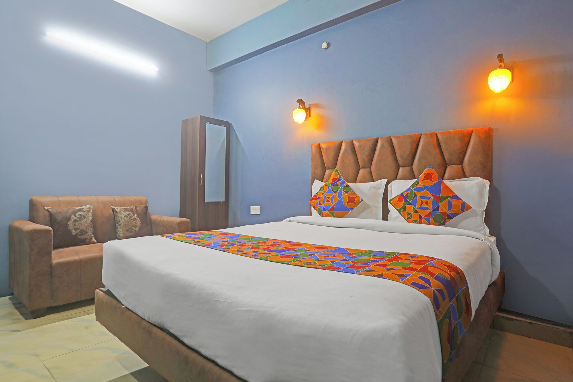 A bedroom with a bed, two pillows, a chair, a mirror, and wall-mounted lights.