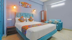 Une chambre à coucher comprenant un lit, un fauteuil recouvert d’un tissu bleu, une armoire en bois et une œuvre d’art accrochée au mur.