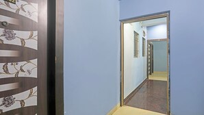 Un couloir avec un mur bleu, une porte en bois ornée de motifs floraux et un miroir qui reflète une porte avec des fenêtres à barreaux.