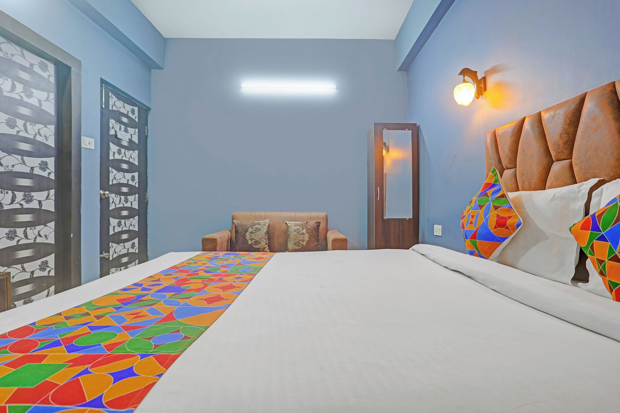 Una habitación de hotel con una cama, una silla, una lámpara de pared y una puerta.