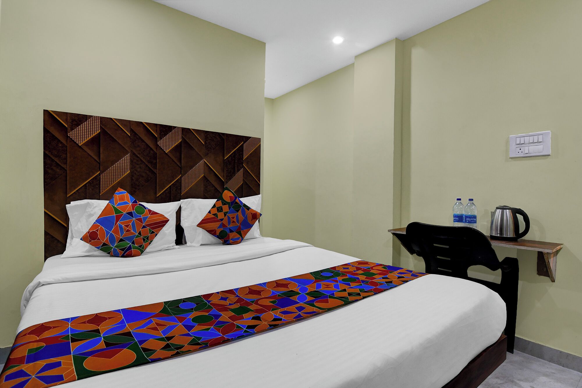 A hotel room with a bed, pillows, a desk, and a chair.