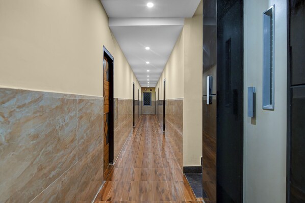 A corridor with tiled walls and a wooden floor, leading to doors with handles. - FabHotel Star Light B - Nr. Rushikonda (Visakhapatnam)
