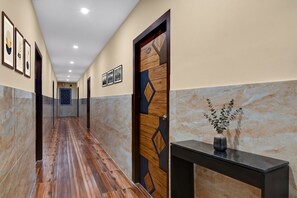 Ein Korridor mit Holzboden, einer Tür mit geometrischen Mustern, gerahmten Bildern an der Wand und einer Konsole mit Pflanzen.