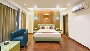 Una camera d'albergo con un letto, una poltrona blu, un tavolino e un condizionatore d'aria.