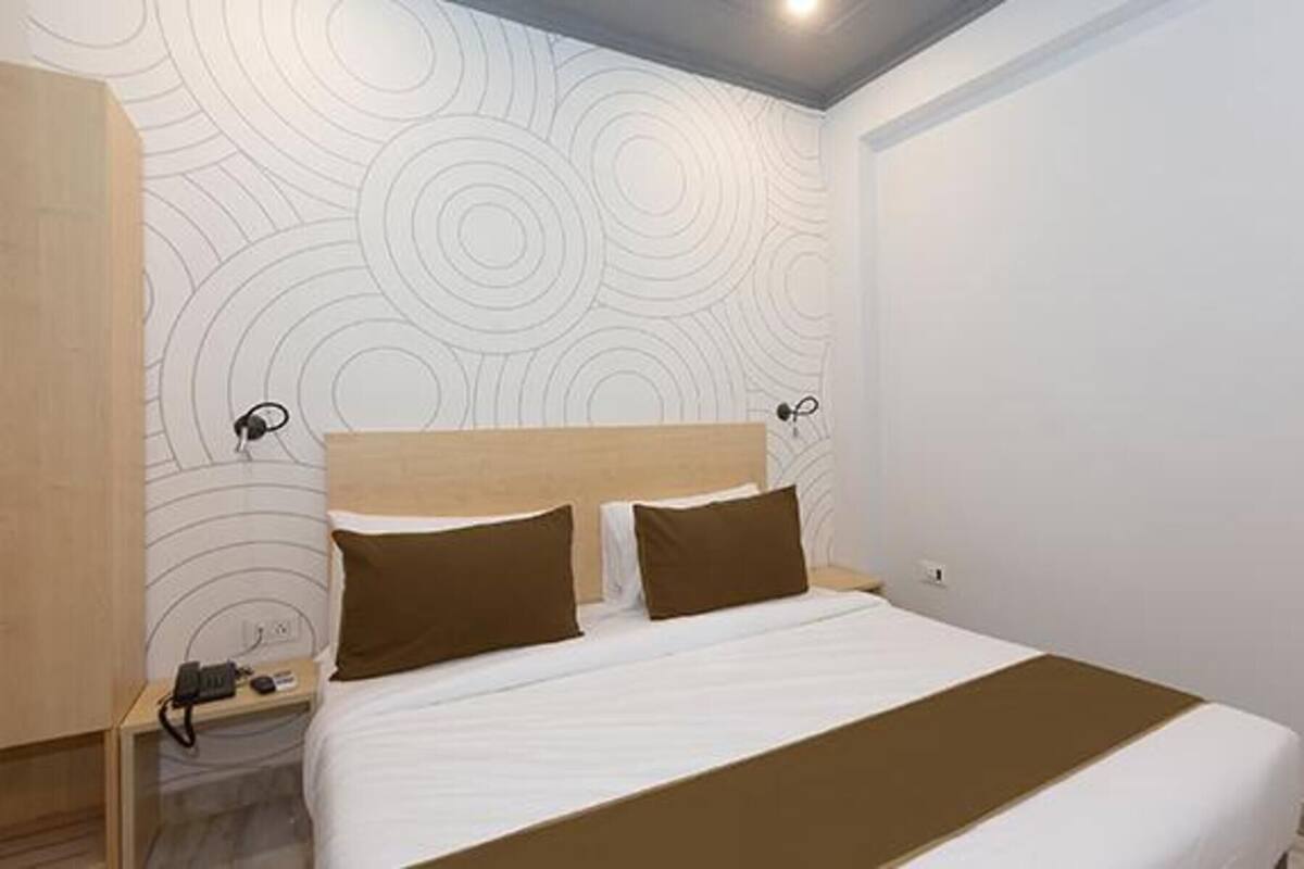A hotel room with a bed, a nightstand, and a wall with a circular pattern.