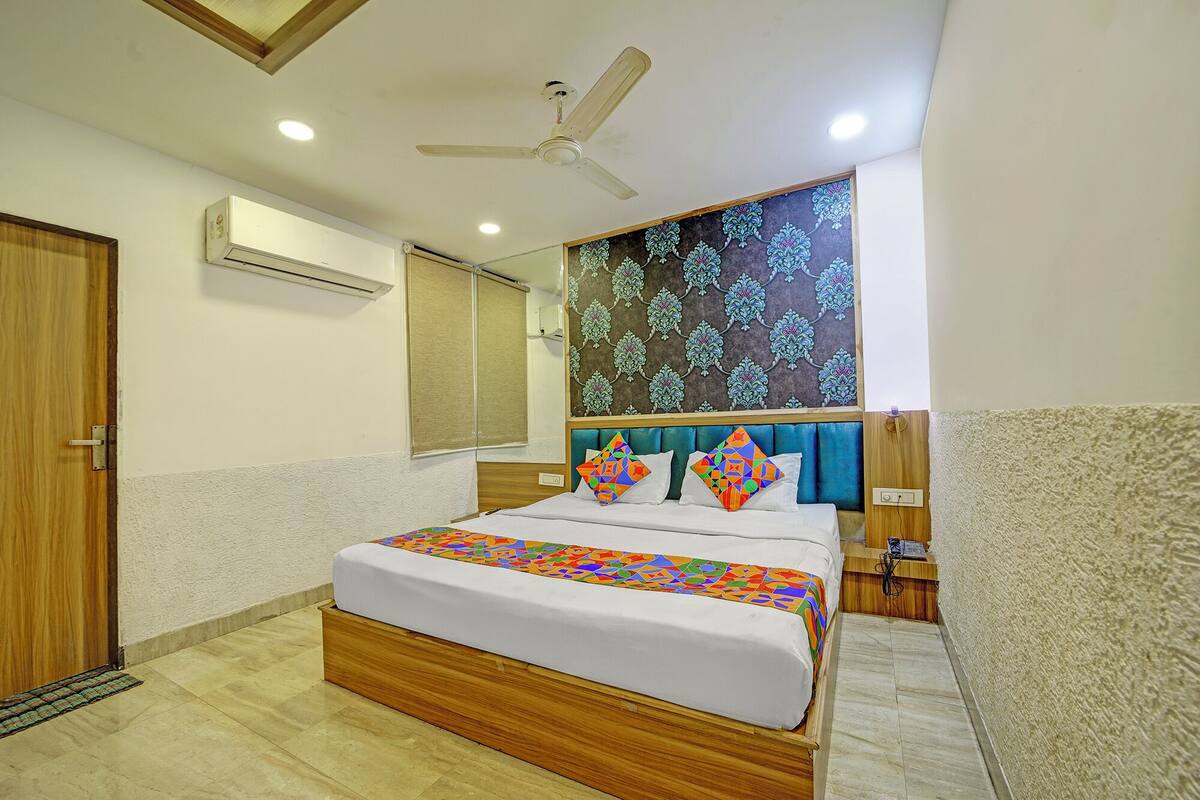 A bedroom with a bed, a ceiling fan, a window with blinds, and a decorative wall panel.