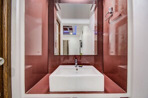 A bathroom with a white sink, a mirror, and a red wall. - Fabexpress Square Inn (Bhopal)