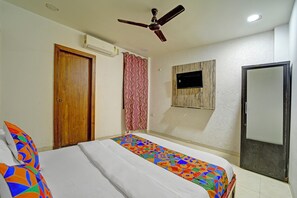 A bedroom with a bed, a ceiling fan, an air conditioner, a TV mounted on the wall, and a door. - Fabexpress Square Inn (Bhopal)