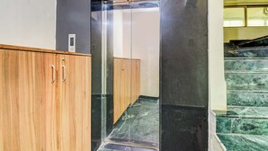 A hallway with a wooden cabinet, a glass elevator, and a marble staircase. - Fabhotel New Pune Residency (Pune)