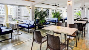 A modern indoor seating area with tables and chairs, large windows, and potted plants. - Fabhotel New Pune Residency (Pune)