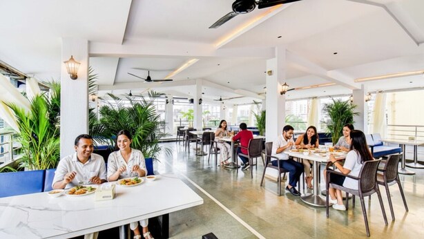 A spacious indoor dining area with multiple tables and chairs, ceiling fans, and large windows allowing natural light. - Fabhotel New Pune Residency (Pune)