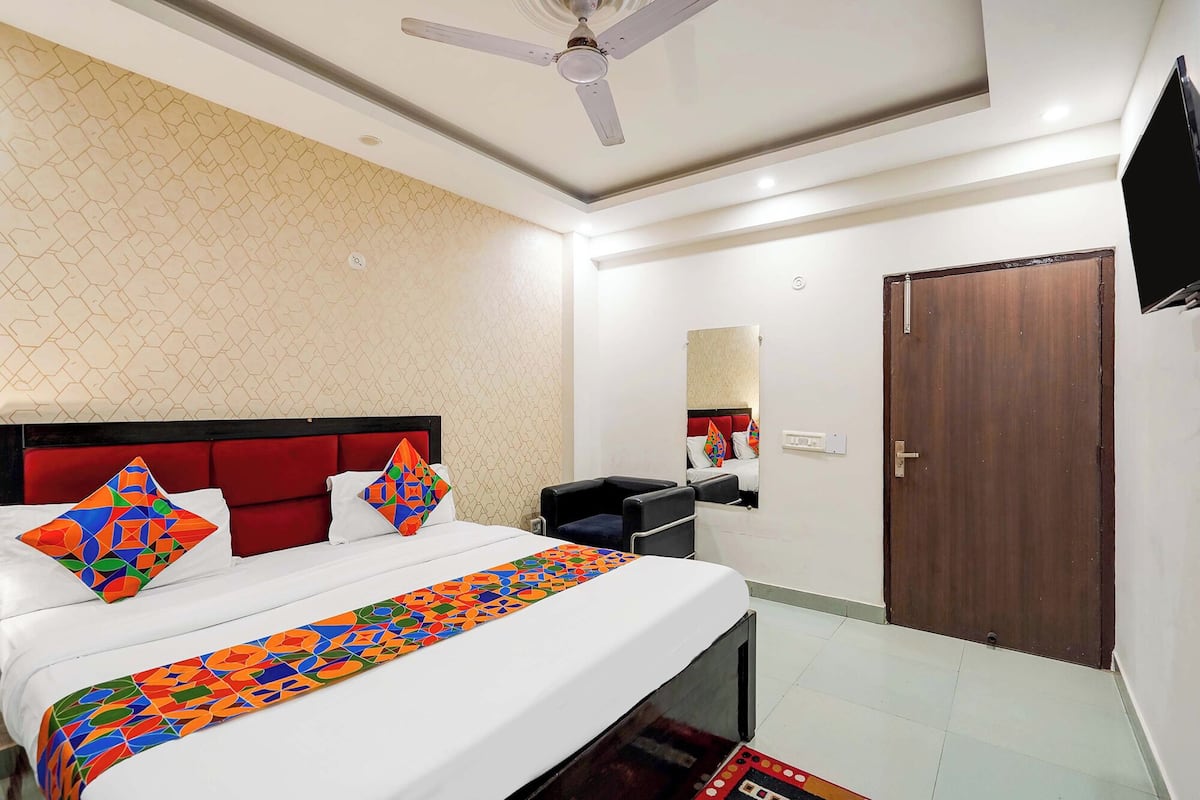 A hotel room with a bed, a ceiling fan, a wooden door, and a mirror on the wall.
