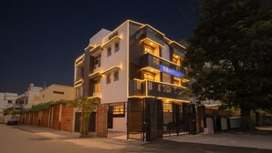 Egy modern, többemeletes épület, amelyen feltűnő „fabHotels” felirat látható, és amelynek erkélyei és egy kapuval ellátott bejárata van.