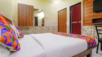 Una cama bien hecha con almohadas coloridas, un armario de madera, una puerta roja y un espejo.
