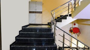 A staircase with black marble steps and metal railings, leading to a landing with a white cabinet and a red fire extinguisher. - Fabexpress Sagar Residency (Panvel)
