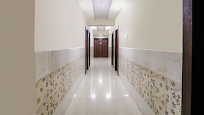 A hallway with a tiled floor and patterned walls, leading to a set of double doors. - Fabexpress Sagar Residency (Panvel)
