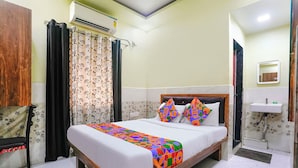 A hotel room with a bed, a wooden wardrobe, a bathroom with a sink, and a shower. - Fabexpress Sagar Residency (Panvel)