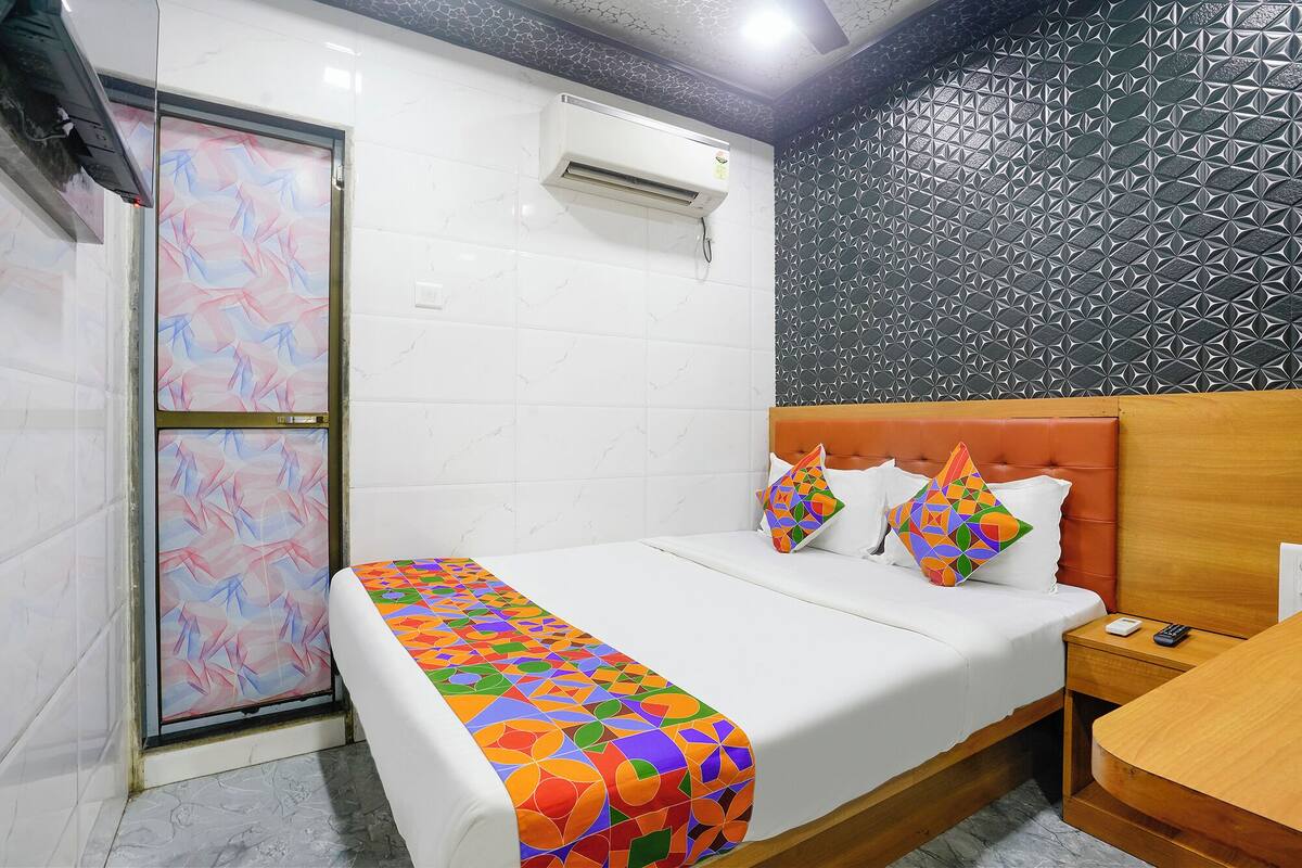 A hotel room with a bed, a bedside table, a nightstand, a window with a view, and a wall with a geometric pattern.
