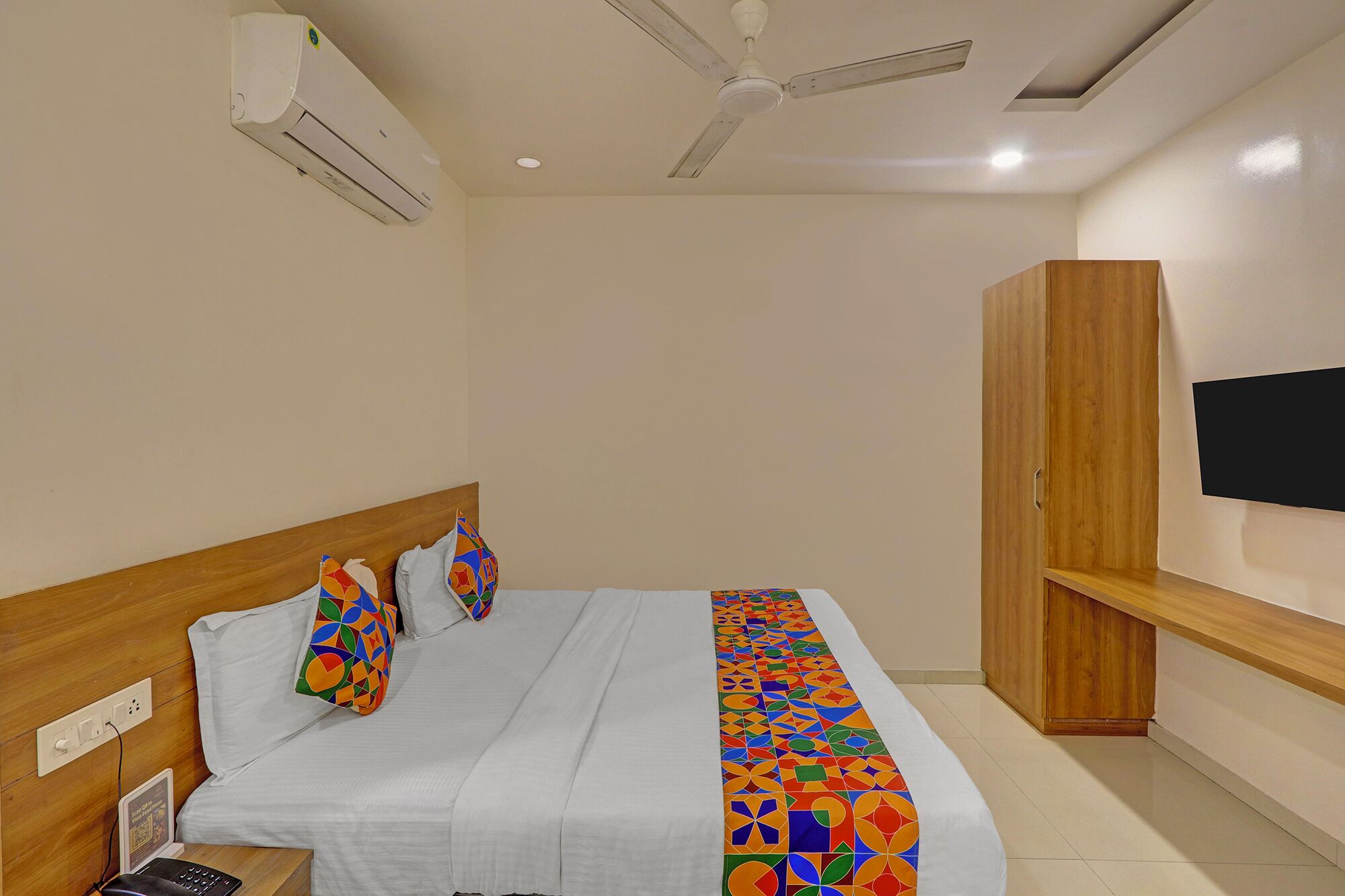 Een slaapkamer met een bed, een houten garderobe, een plafondventilator en een tv aan de muur.