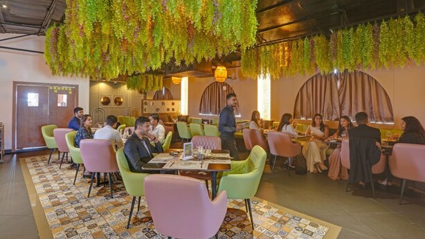 Un restaurante con sillas, mesas y plantas colgantes de colores.