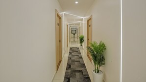 Un pasillo moderno de hotel con una recepción al fondo, suelo de baldosas y plantas en macetas.
