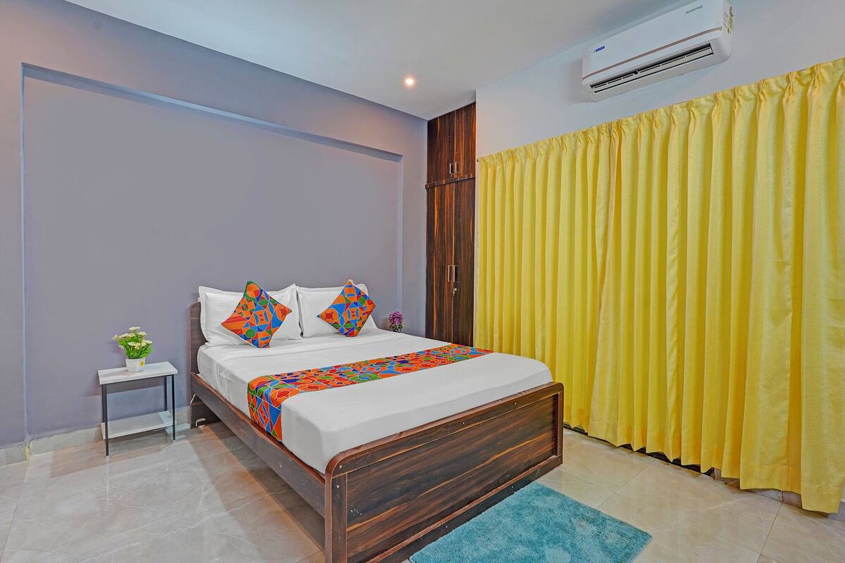 A bedroom with a wooden bed, a small bedside table, a potted plant, and a yellow curtain.