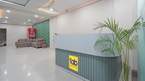 A hotel reception area with a modern design, featuring a reception desk with a logo, a seating area with sofas, and a staircase in the background. - Fabhotel Elite Inn I (Indore)