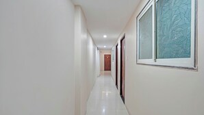 A hallway with a wooden door at the end, a window with a textured pattern, and a tiled floor. - Fabhotel Elite Inn I (Indore)