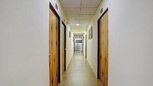 A narrow hallway with wooden doors on both sides, leading to a room with a bed and a window. - Fabhotel Nova Rooms (Surat)