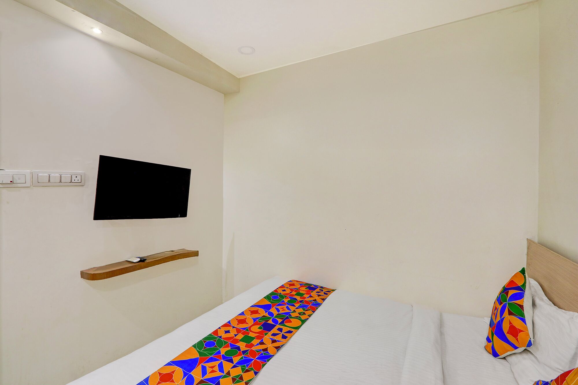 A hotel room with a bed, a TV mounted on the wall, and a power outlet.