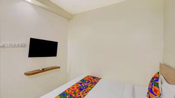 A hotel room with a bed, a TV mounted on the wall, and a power outlet.