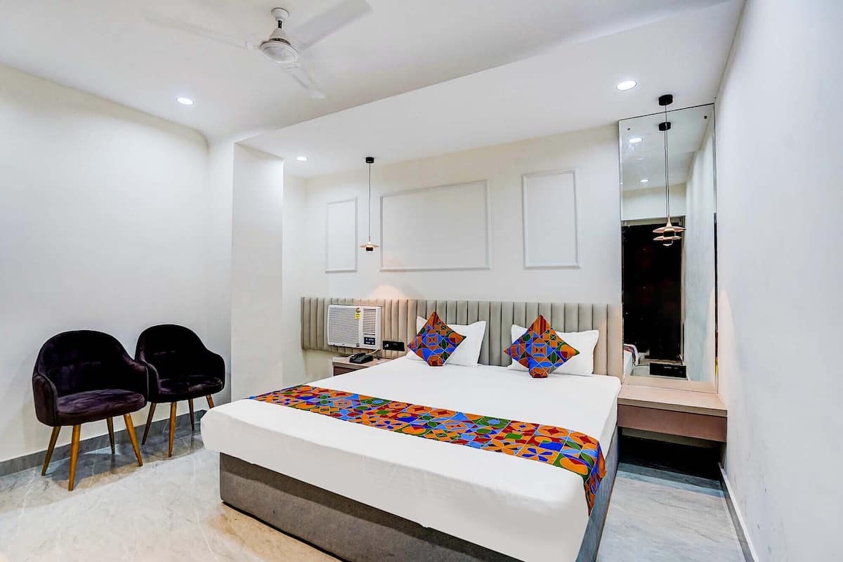 Une chambre moderne avec un grand lit, deux fauteuils, une table de chevet et un miroir.