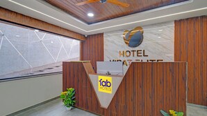 A hotel reception desk with a wooden finish, a marble wall, and a ceiling fan. - Fabhotel Virat Elite (Hyderabad)