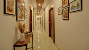 A hallway with framed artworks on the walls, a wooden table with a vase and candle, and a polished floor. - Fabhotel Virat Elite (Hyderabad)