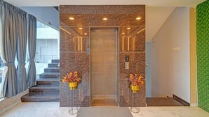 An elevator entrance with a granite wall, two flower stands, and a staircase to the left. - Fabhotel Virat Elite (Hyderabad)
