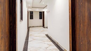 A hallway with a marble floor, white walls, and wooden paneling on the sides. - Fabhotel Golden Inn (Noida)