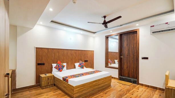 A modern bedroom with a wooden headboard, a bed with colorful pillows, a ceiling fan, and an air conditioning unit. - Fabhotel Golden Inn (Noida)